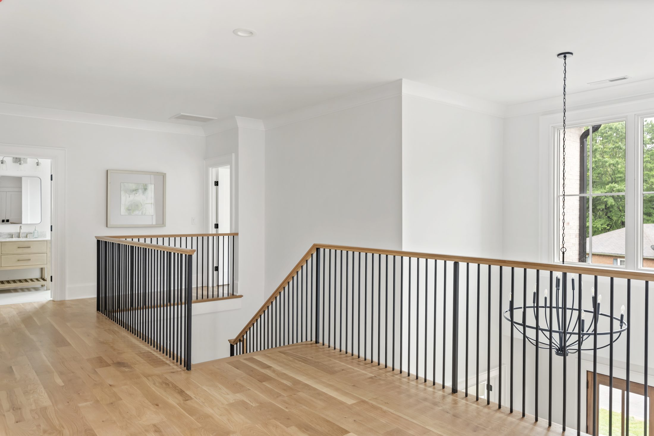Upstairs landing with white oak floors, iron-spindle railing, and orb chandelier overlooking the foyer — Bywood by Stillman Properties Charlotte NC