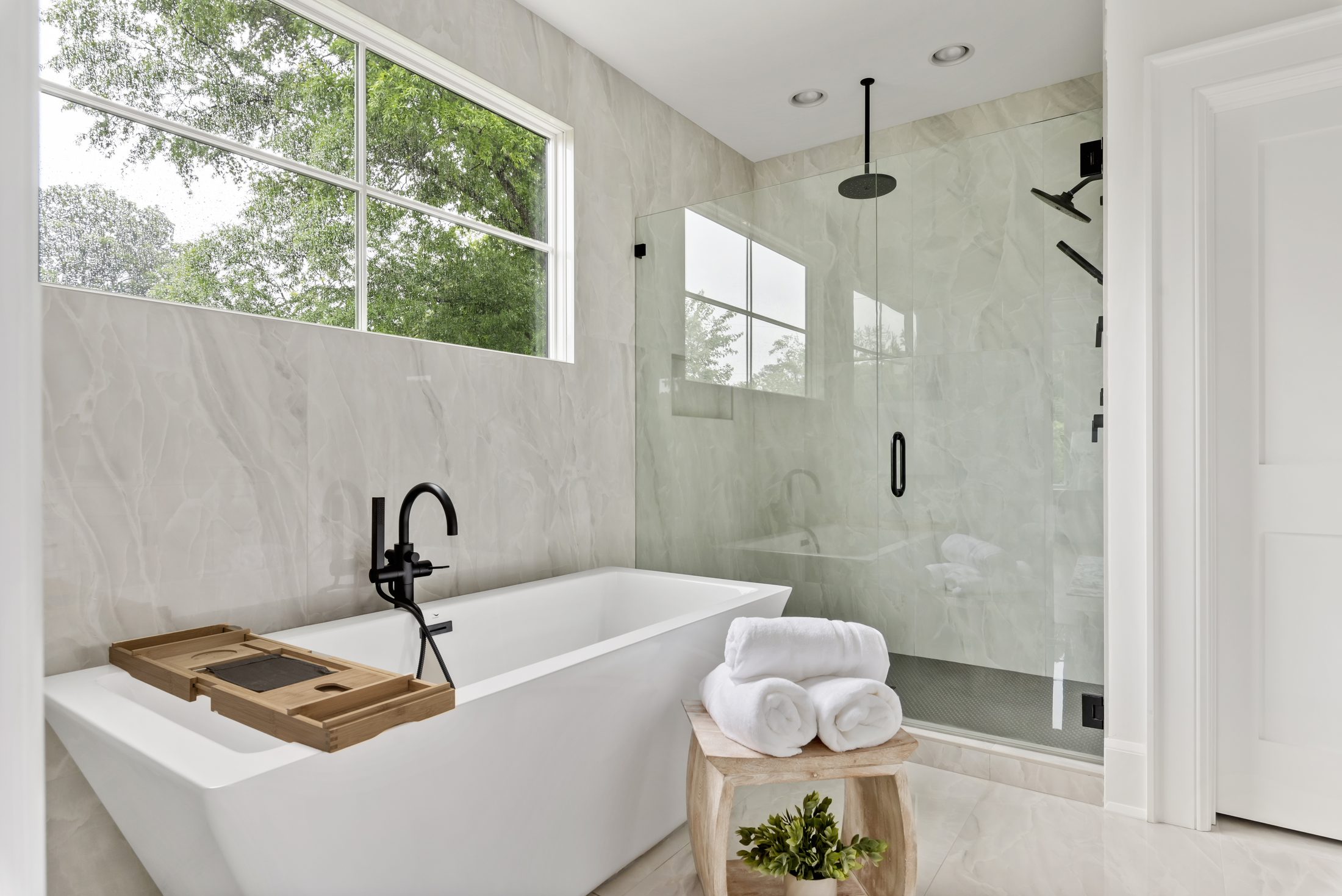 Primary spa bath freestanding tub beneath a marble-look tile wall with natural light — Bywood by Stillman Properties Charlotte NC
