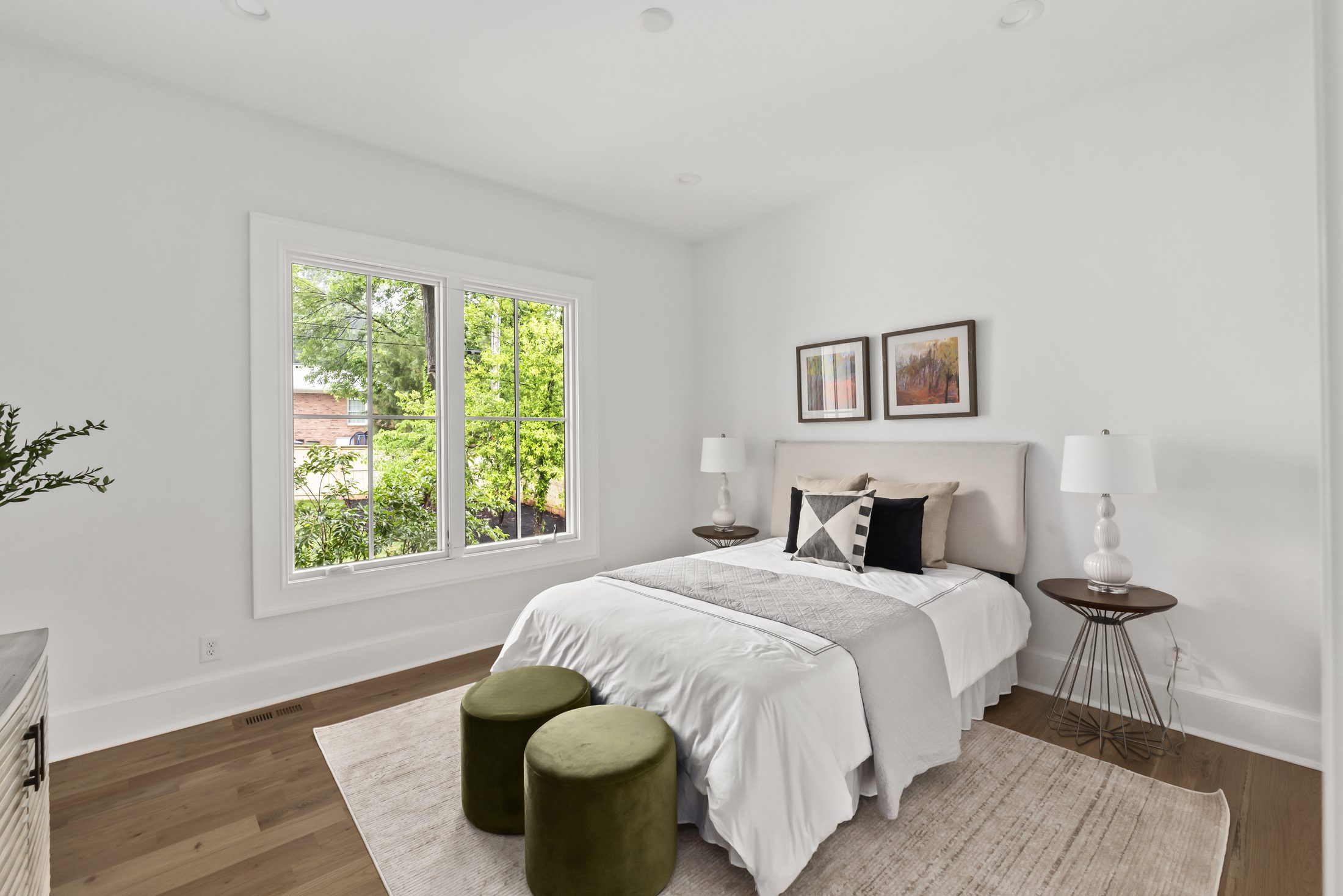 Secondary bedroom with white bedding, framed art, and green accent ottomans — Bywood by Stillman Properties Charlotte NC