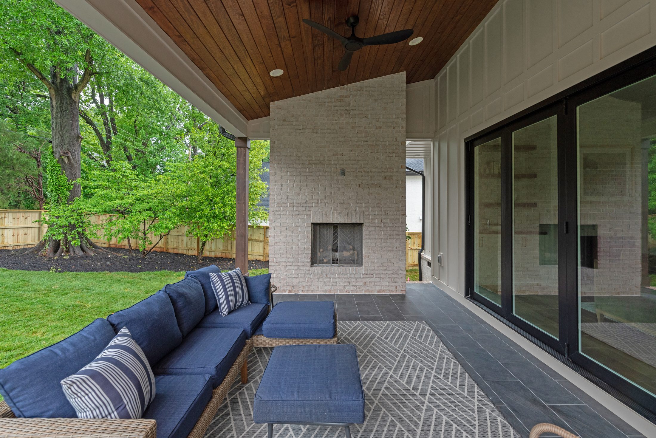 Floor-to-ceiling whitewashed brick outdoor fireplace beneath the cedar porch ceiling — Bywood by Stillman Properties Charlotte NC