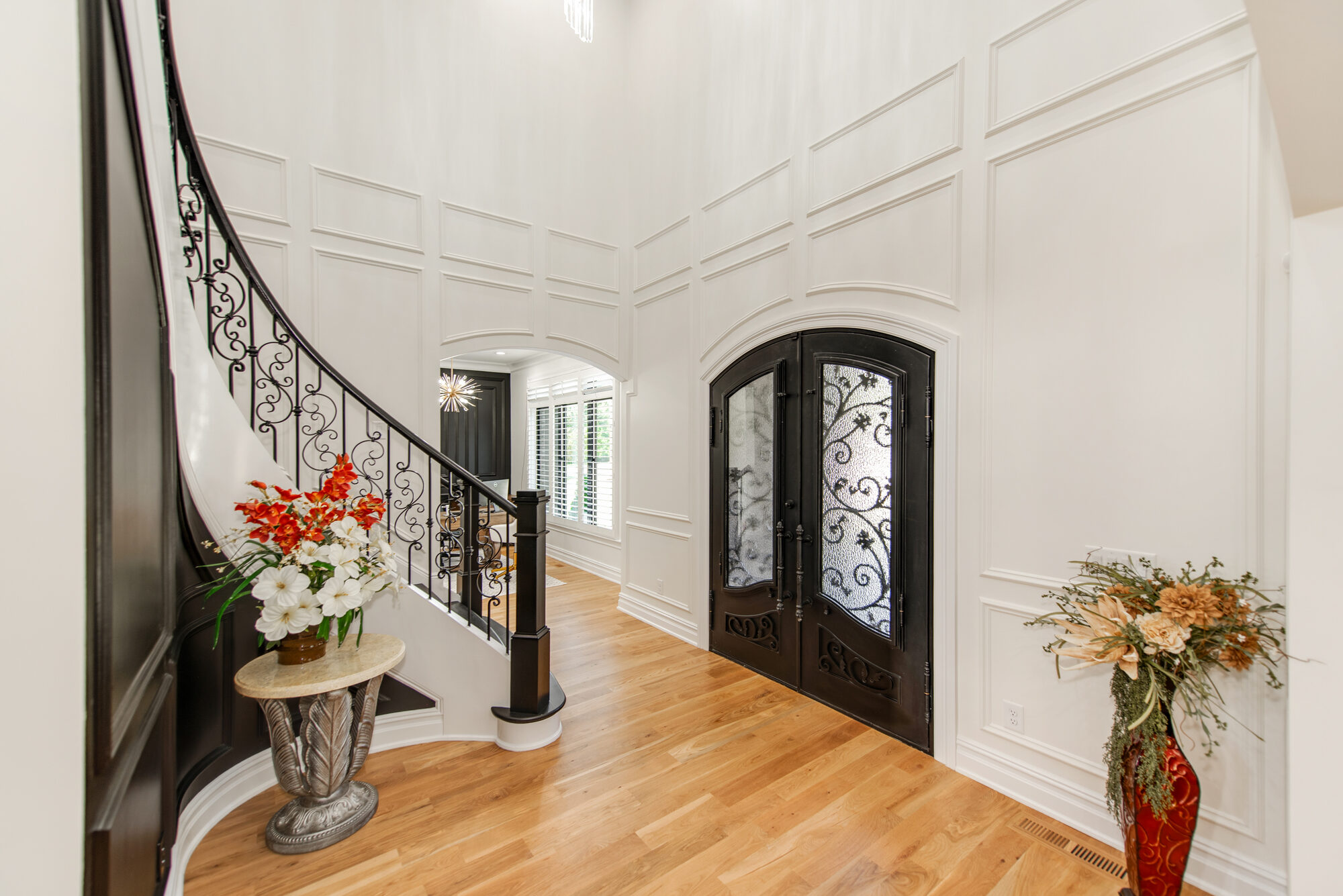 Two-story foyer at Coddle Creek with curved iron staircase, custom millwork wainscoting, and arched iron entry doors — Stillman Properties Concord NC
