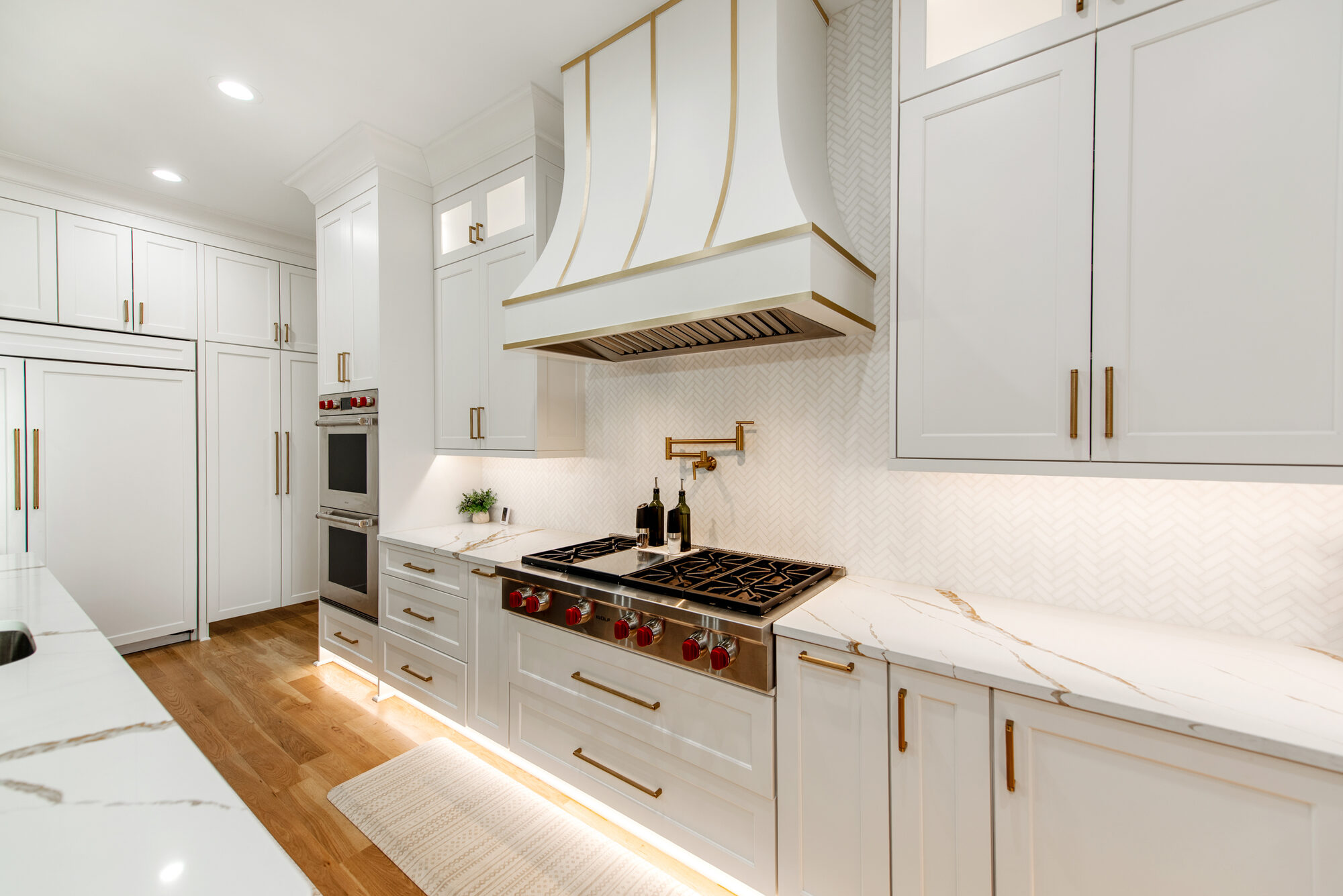 Kitchen range wall with Wolf six-burner range, custom hood with brass detailing, and herringbone backsplash — Coddle Creek by Stillman Properties Concord NC