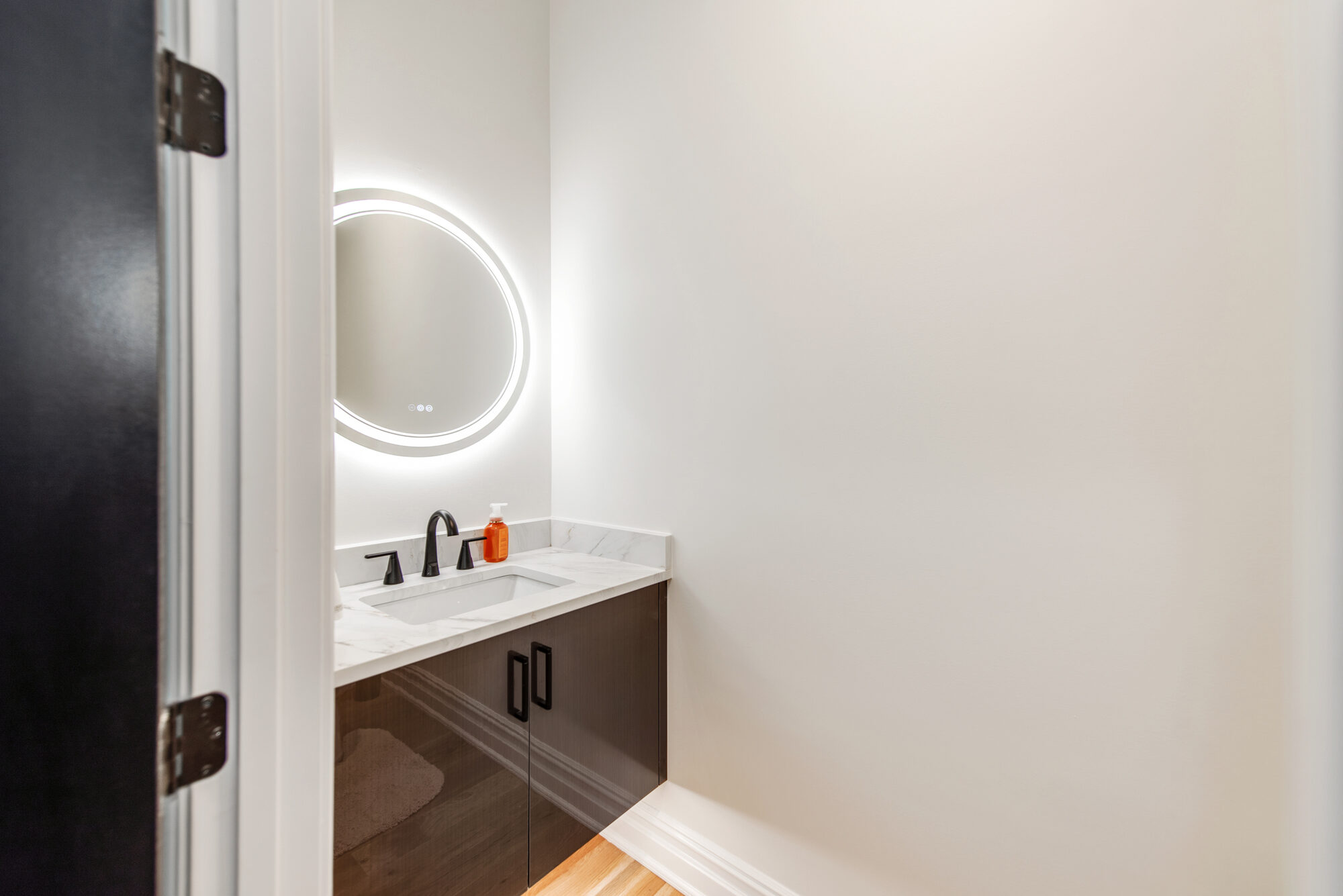 Powder bath with backlit round mirror, dark walnut floating vanity, and matte black fixtures — Coddle Creek by Stillman Properties Concord NC