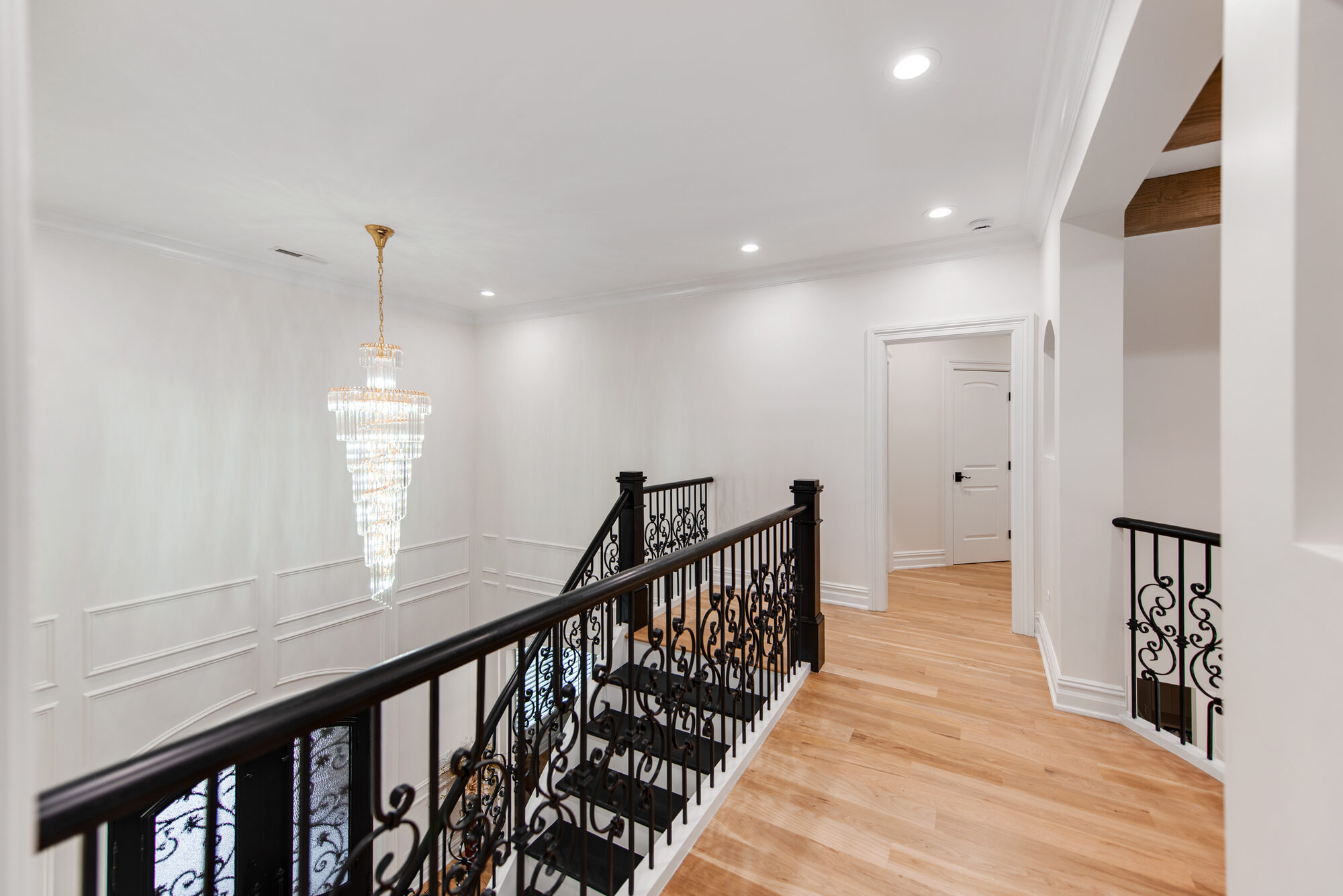 Upstairs hall with cascading crystal chandelier above the curved staircase — Coddle Creek by Stillman Properties Concord NC