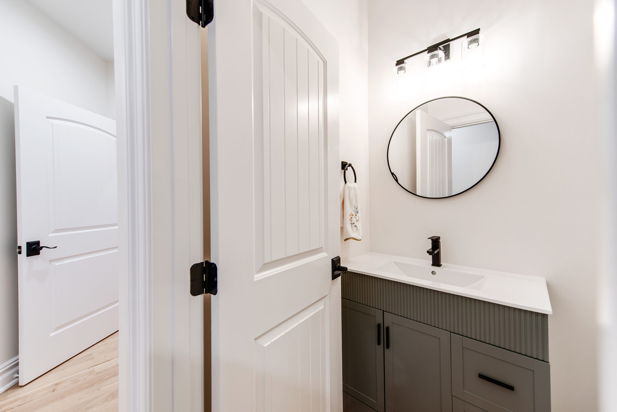 Guest powder room with fluted dark cabinetry, round black mirror, and matte black fixtures — Coddle Creek by Stillman Properties Concord NC