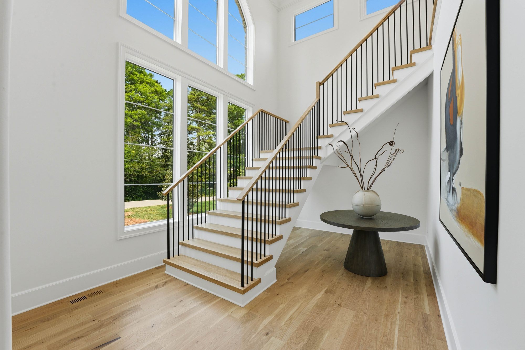 Two-story staircase with white oak treads and iron spindles beneath a cathedral-arched window — Creola custom home in Charlotte NC by Stillman Properties