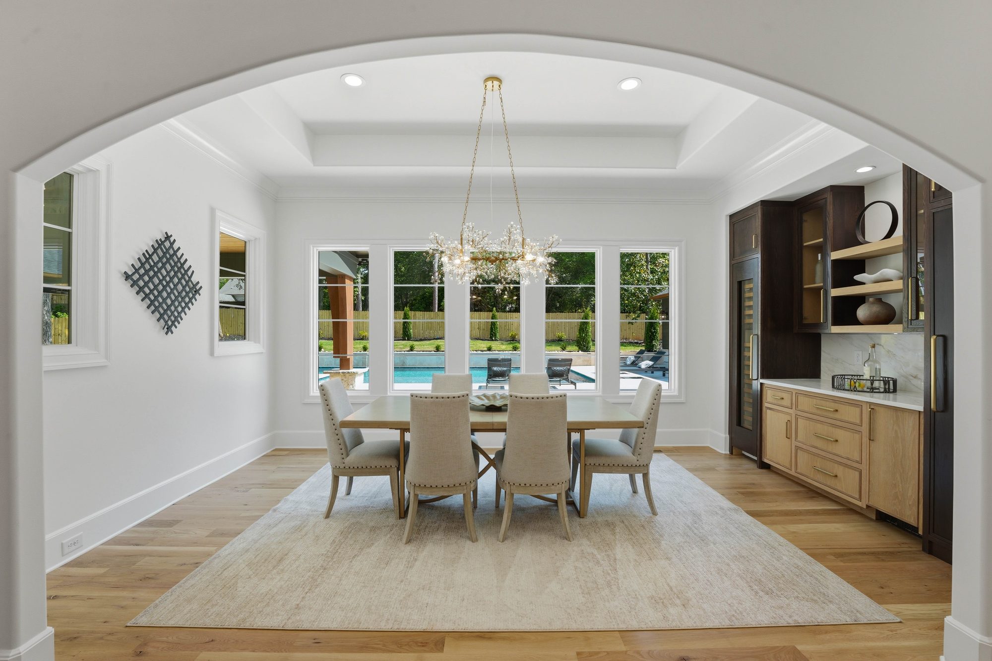 Dining room beneath arched entry with crystal floral chandelier and pool view — Creola custom home in Charlotte NC by Stillman Properties