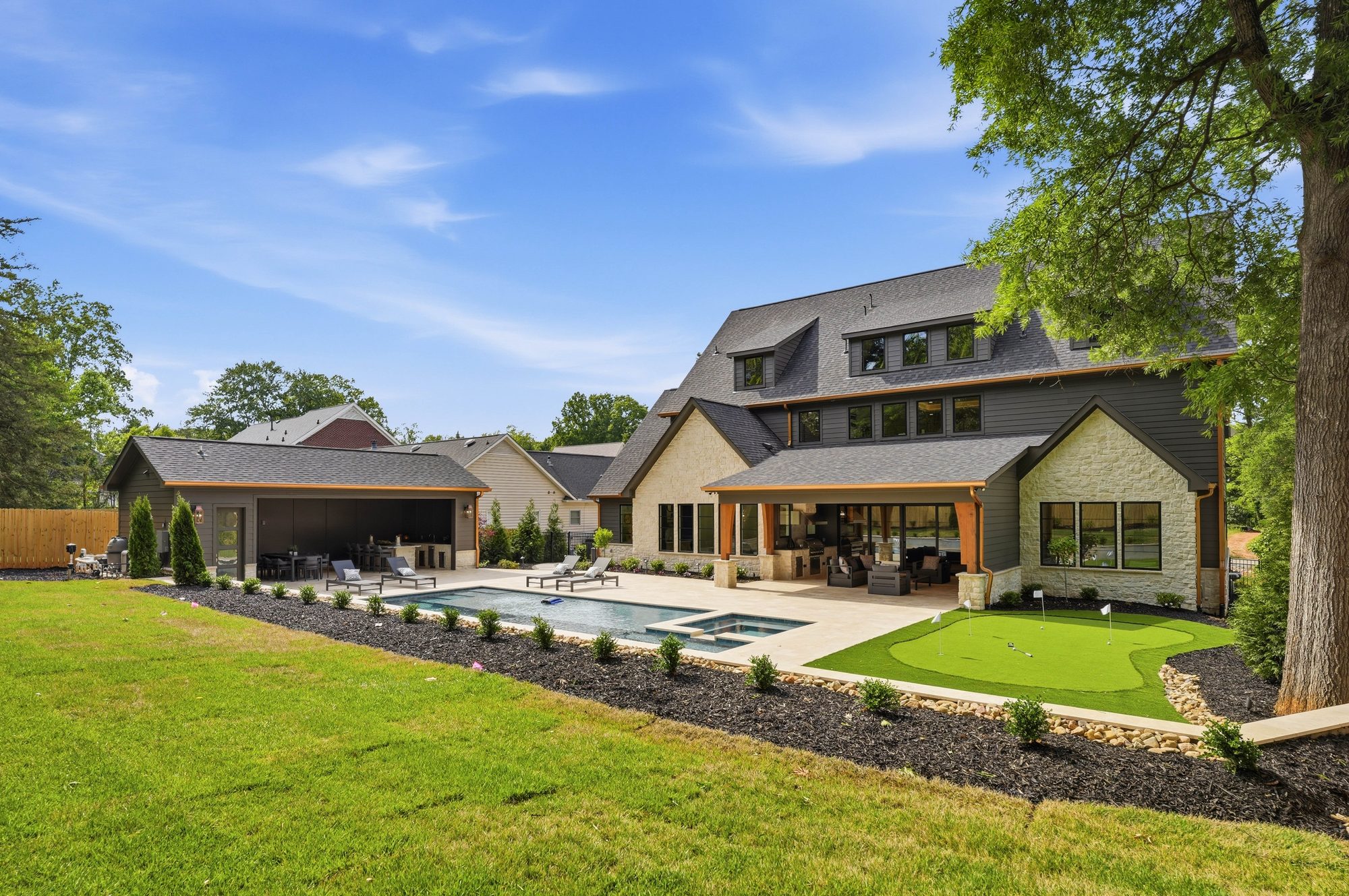 Wide rear view showing cabana, pool, main house, and putting green in a single composition — Creola custom home in Charlotte NC by Stillman Properties