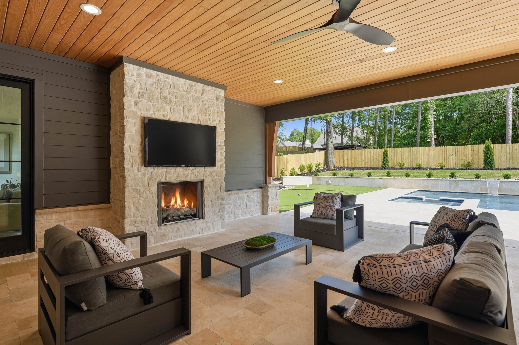 Covered outdoor living room with daytime fireplace lit, sectional seating, and view to pool — Creola custom home in Charlotte NC by Stillman Properties
