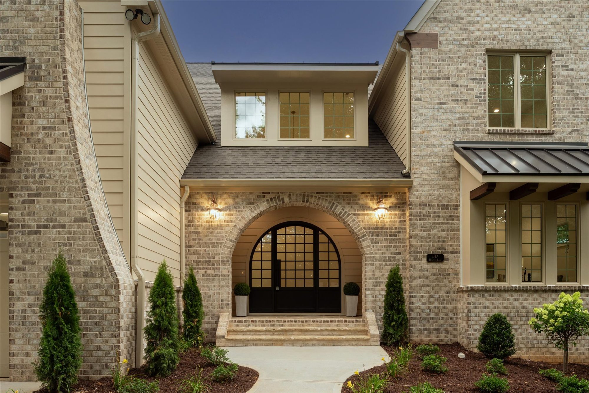 Arched brick entry at Heather with divided-light double doors, lantern sconces, and brick steps at dusk — Heather by Stillman Properties Charlotte NC