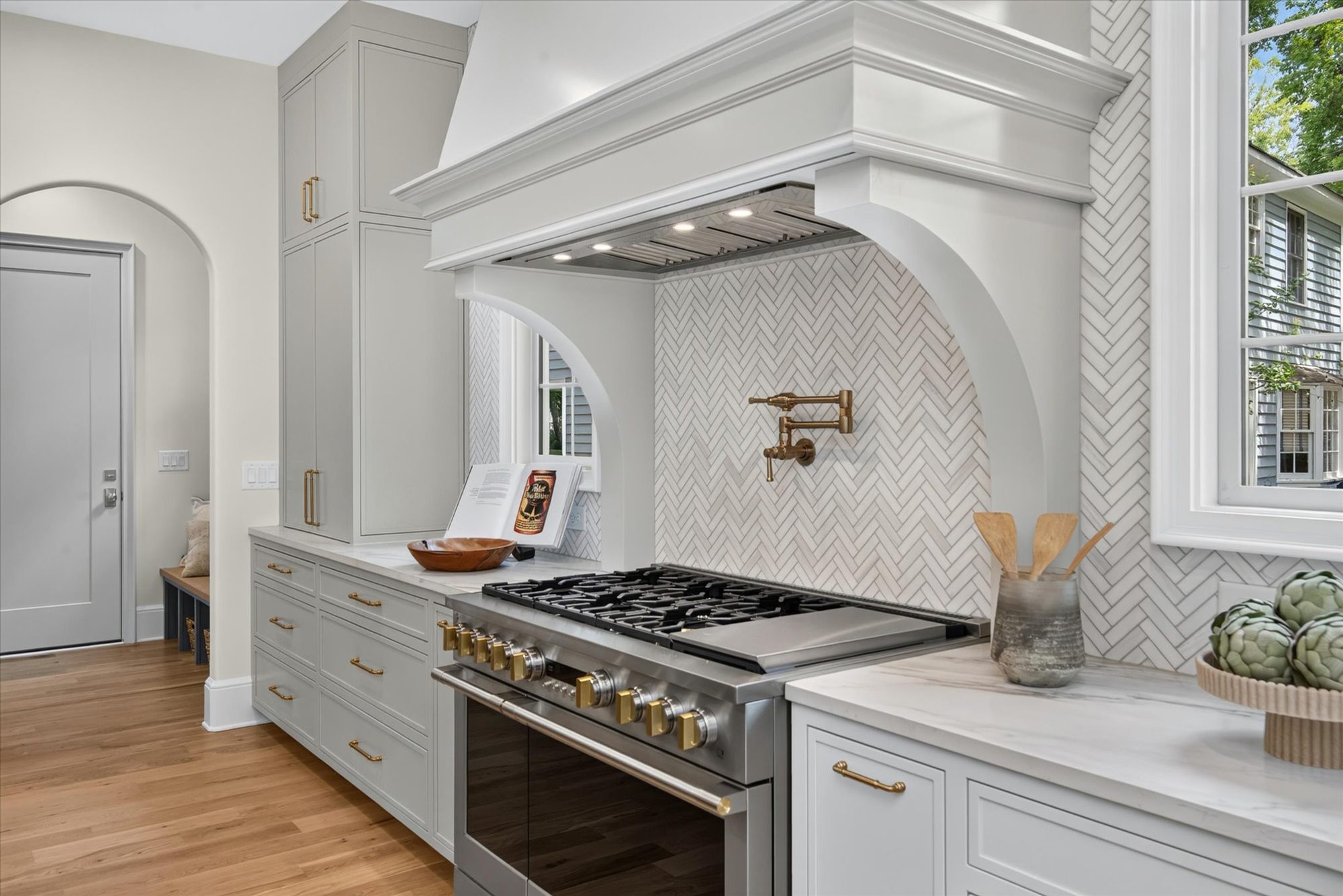 Range wall detail at Heather with professional gas range, brass pot filler, custom plaster hood, and marble herringbone tile — Heather by Stillman Properties Charlotte NC