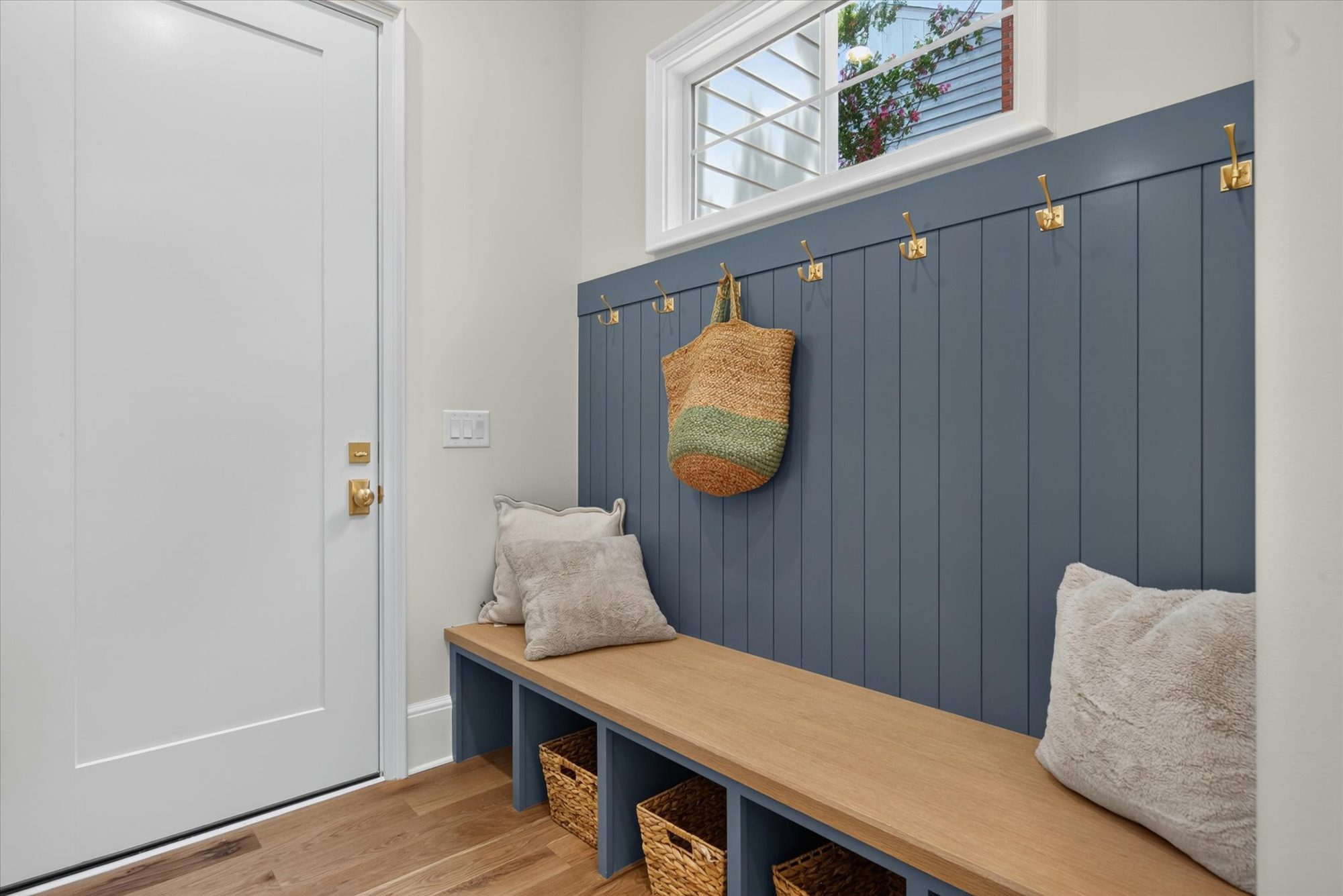 Drop zone at Heather with navy vertical shiplap, white oak bench, brass hooks, and woven basket cubbies — Heather by Stillman Properties Charlotte NC