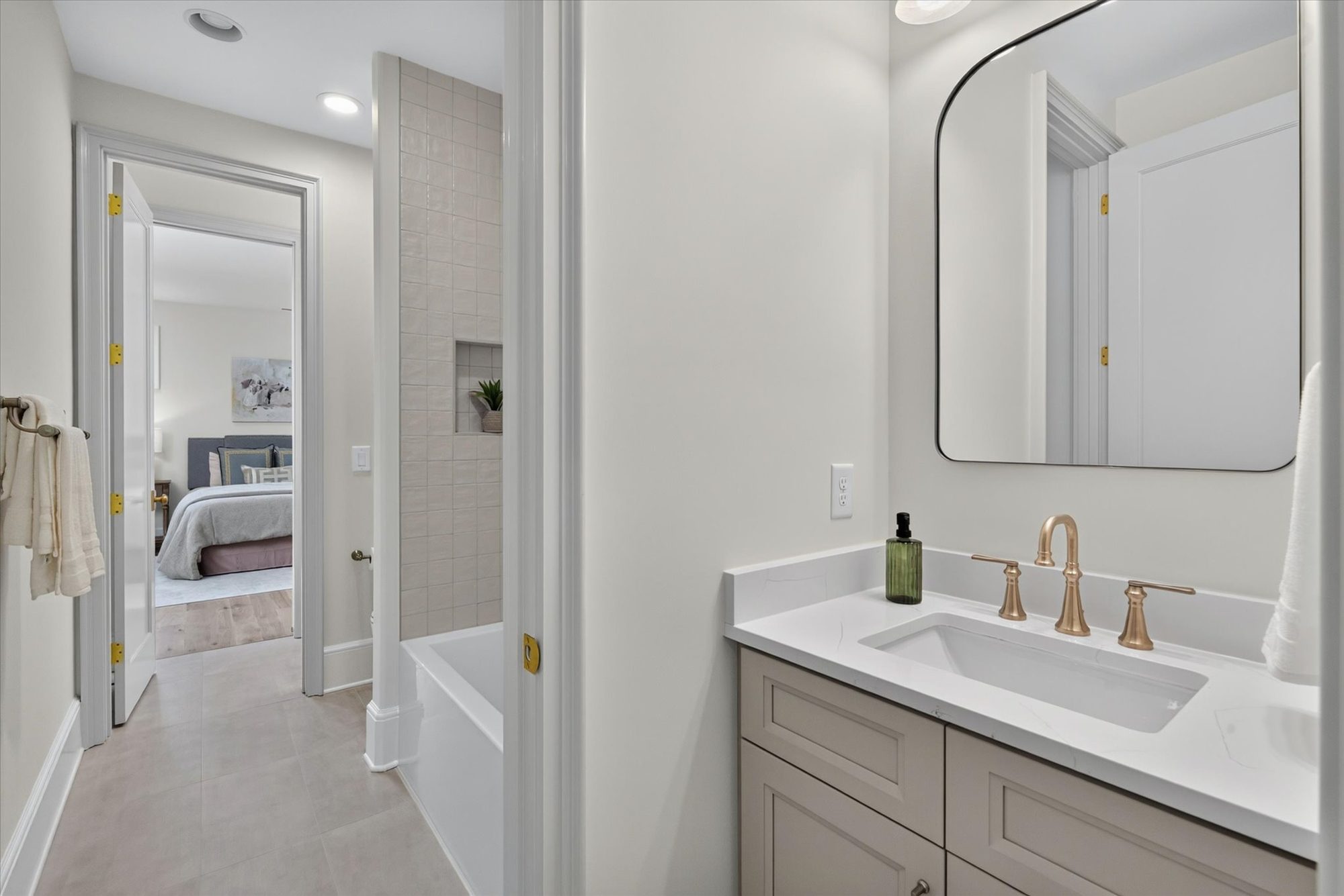 En-suite bath at Heather with quartz-topped vanity, brass fixtures, arched mirror, and tiled tub-shower — Heather by Stillman Properties Charlotte NC