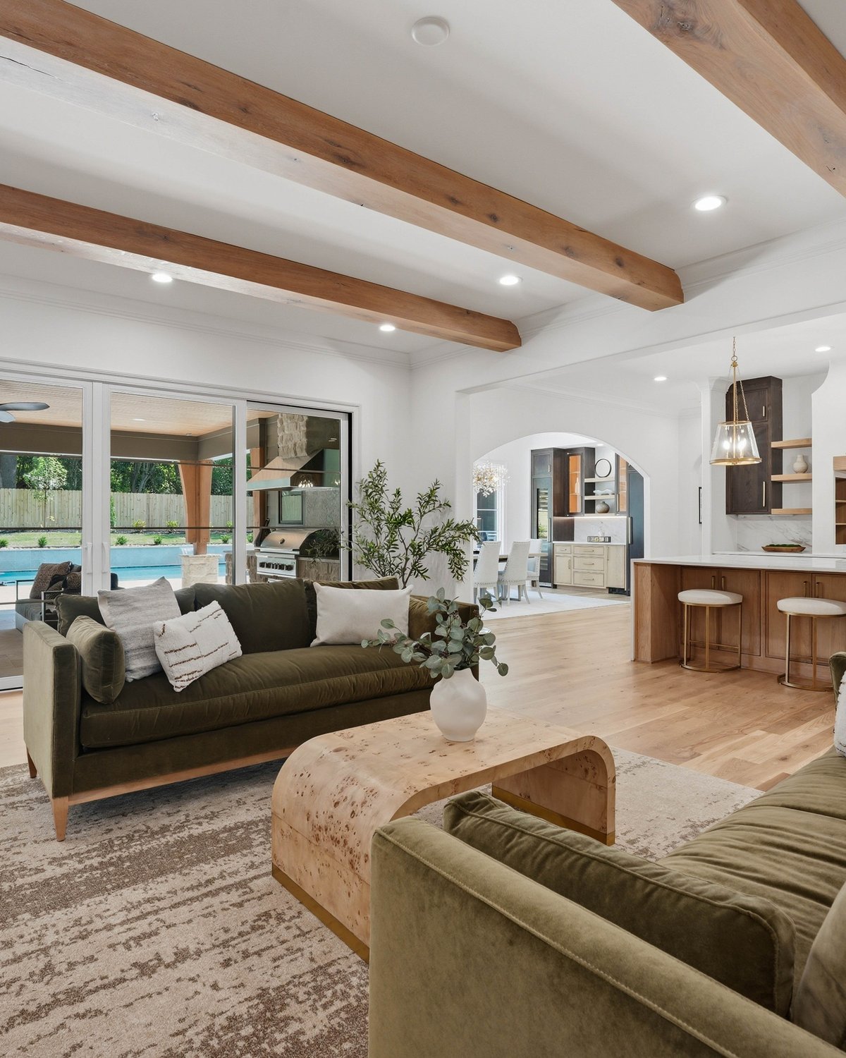 Open-concept great room and kitchen by Stillman Properties — exposed white oak ceiling beams, marble backsplash, and pool views