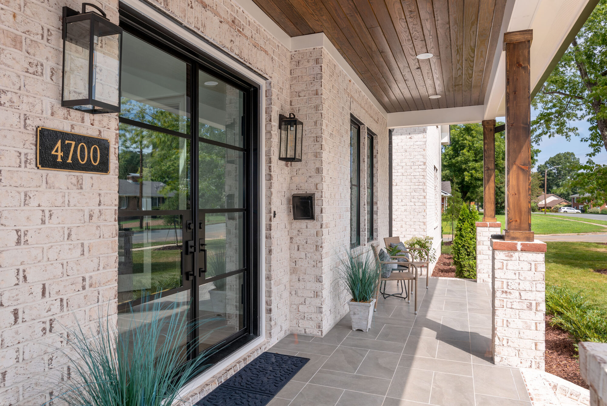 Walker entry detail with black steel-framed glass door, brass address plaque, and lantern sconces — Stillman Properties Cotswold Charlotte NC