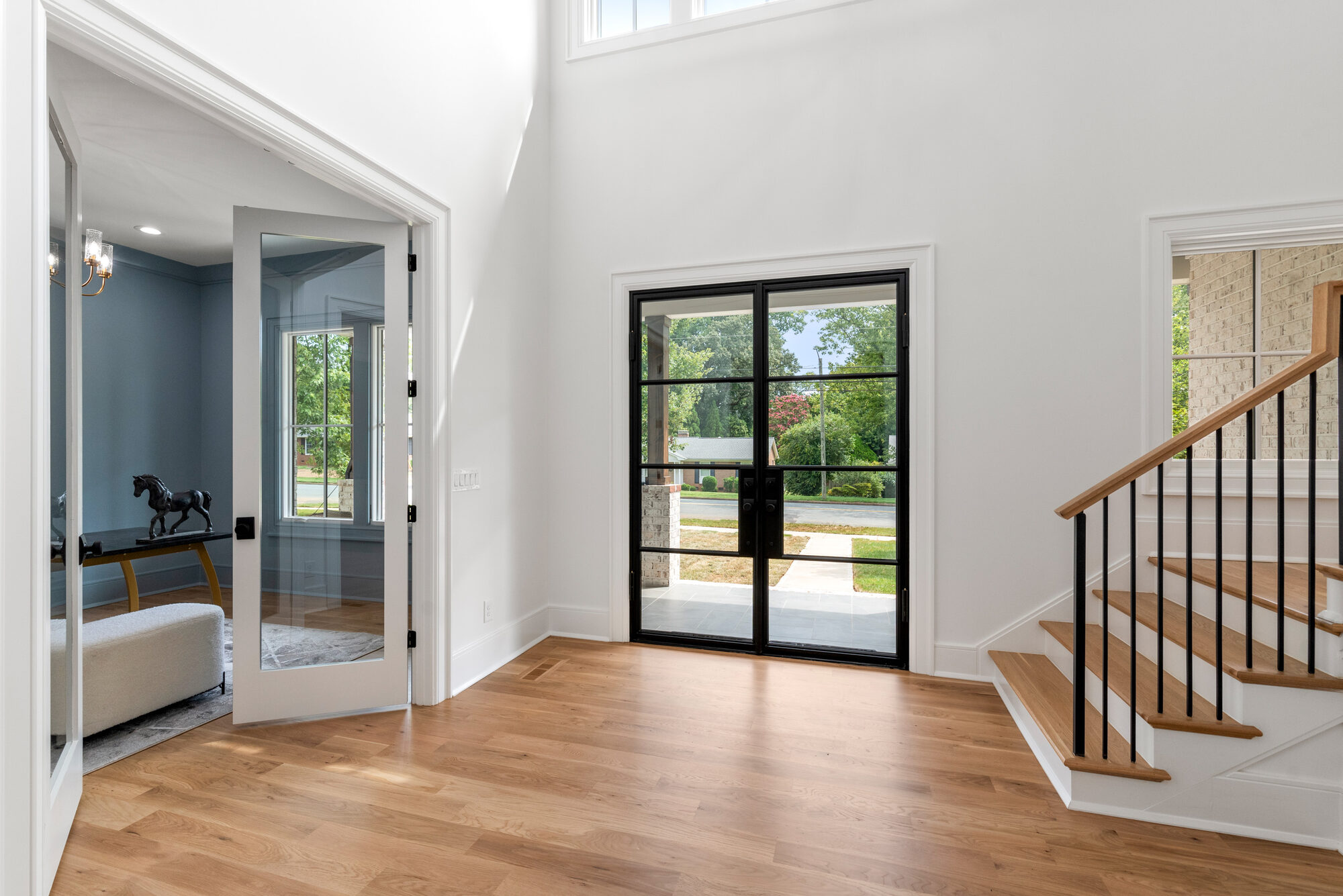Two-story Walker foyer with steel-framed glass doors and white oak staircase with black iron spindles — Stillman Properties Cotswold Charlotte NC