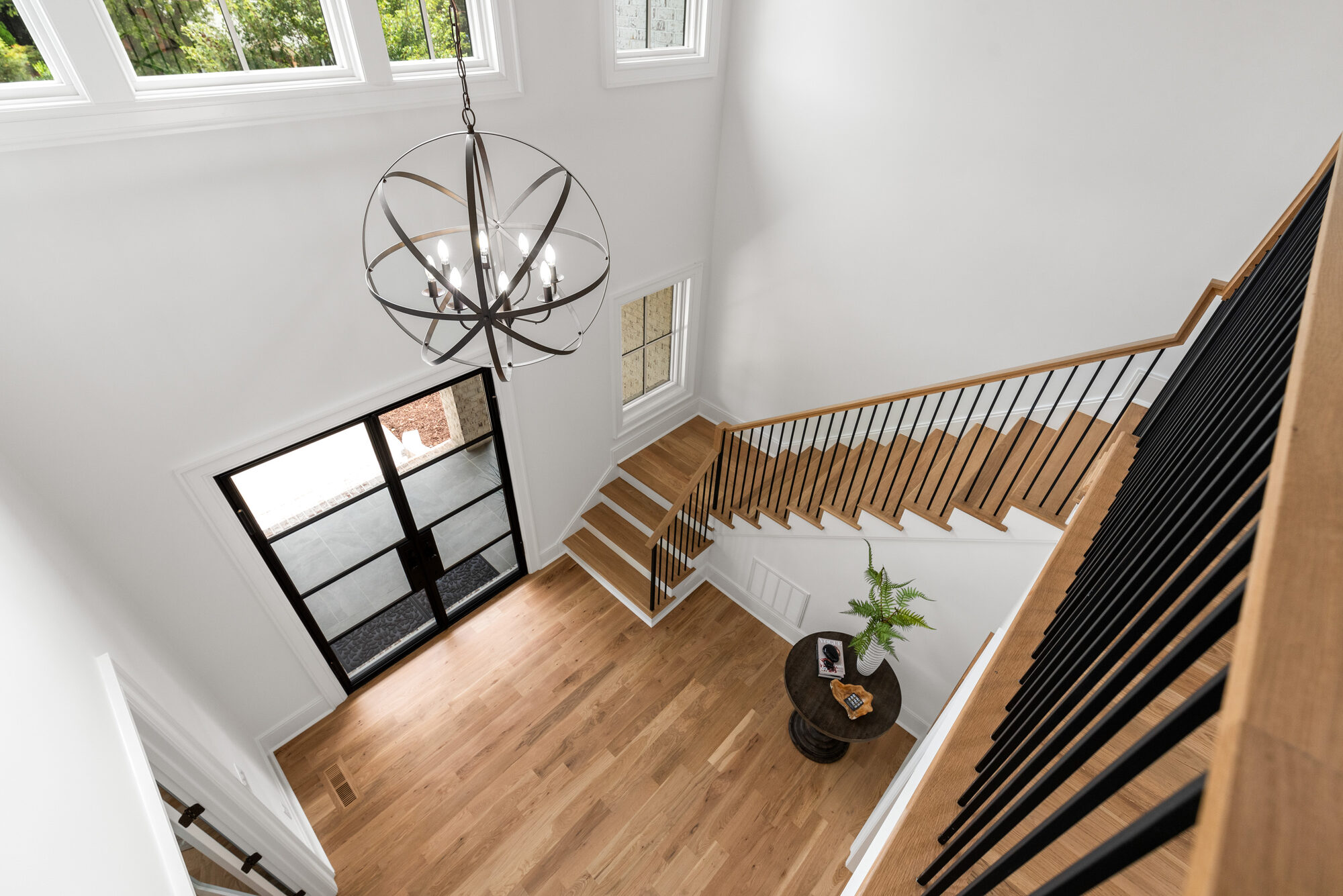 Walker foyer viewed from the upper landing with iron orb chandelier and steel entry doors below — Stillman Properties Cotswold Charlotte NC