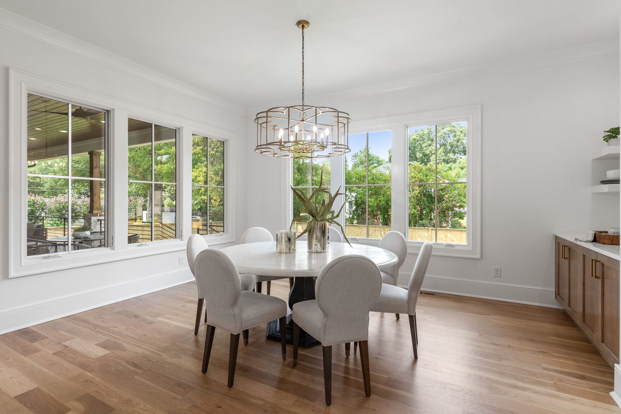 Walker breakfast room with wraparound windows, antique brass chandelier, and views to the covered deck — Stillman Properties Cotswold Charlotte NC