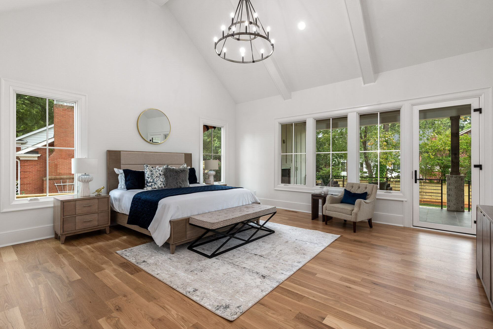 Walker primary bedroom with vaulted ceiling, iron wagon-wheel chandelier, and French doors to a private deck — Stillman Properties Cotswold Charlotte NC