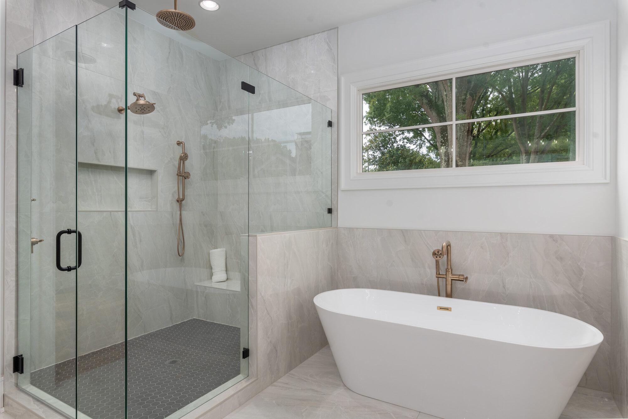 Walker primary spa bath with glass-enclosed marble shower, freestanding tub, and brass tub filler — Stillman Properties Cotswold Charlotte NC